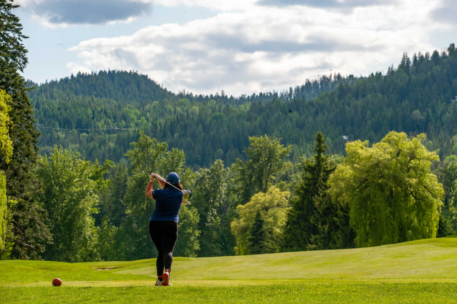 Golfer watching their tee shot fly down a mountain fairway